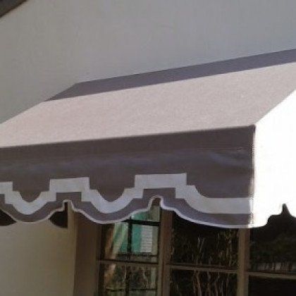 A taupe fabric window awning with a decorative white scalloped trim and border.
