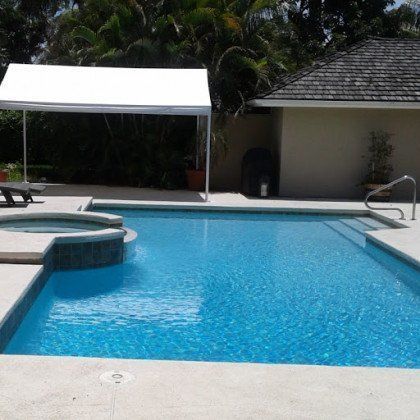 A backyard swimming pool with a raised hot tub and a white canopy tent on a stone patio next to a house.