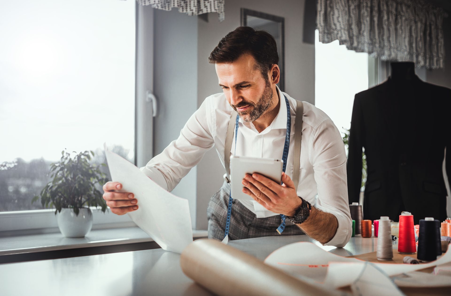 A man is looking at a piece of paper while using a tablet.