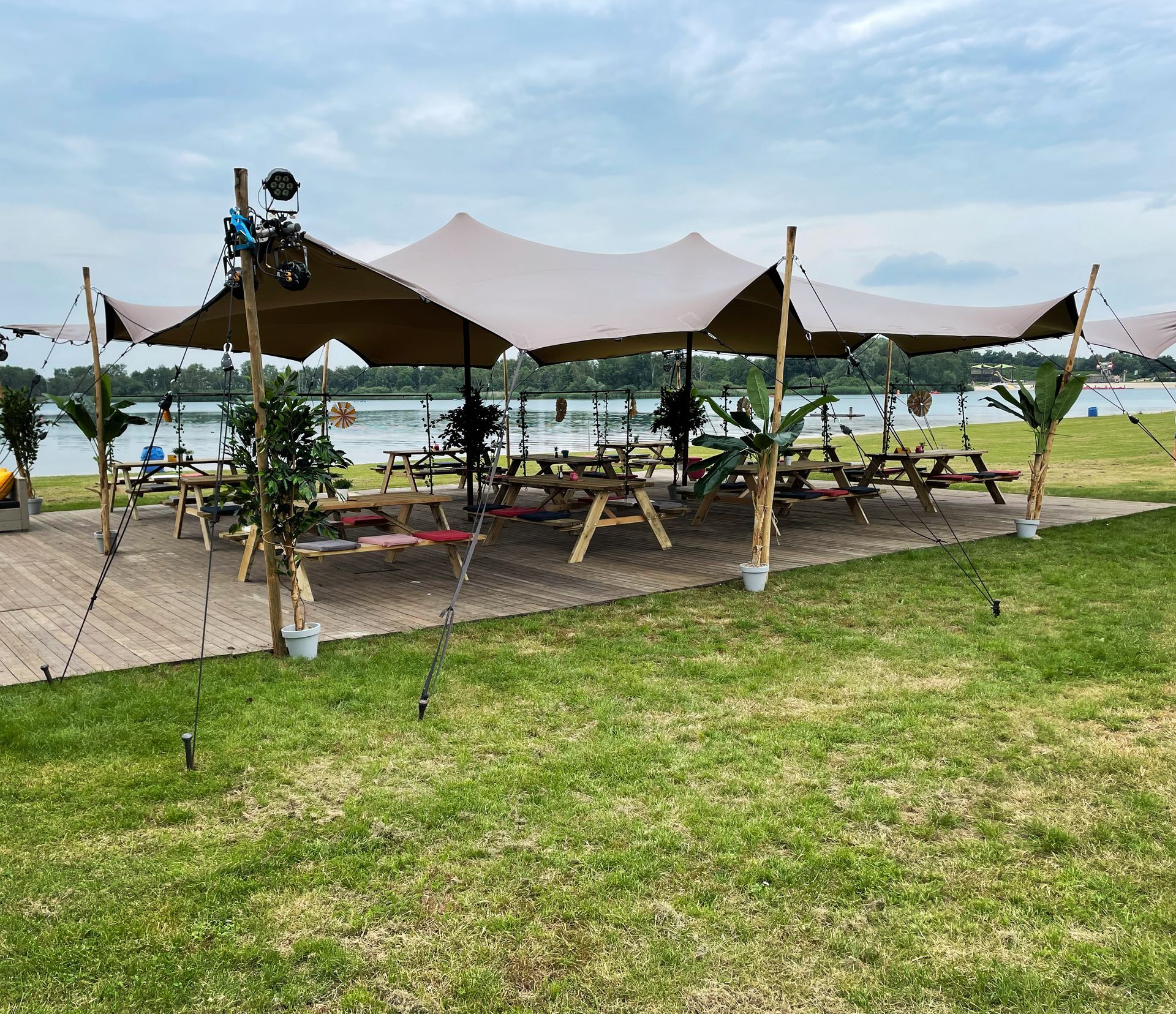 Eetgedeelte buiten met een beige stoffen stretchtent, picknicktafels en uitzicht op het meer.