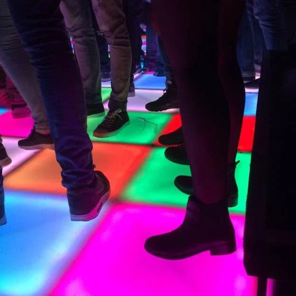 DJ-setup onder een tent met speakers, verlichting en een tafel die verlicht is in geel, blauw, rood en groen.