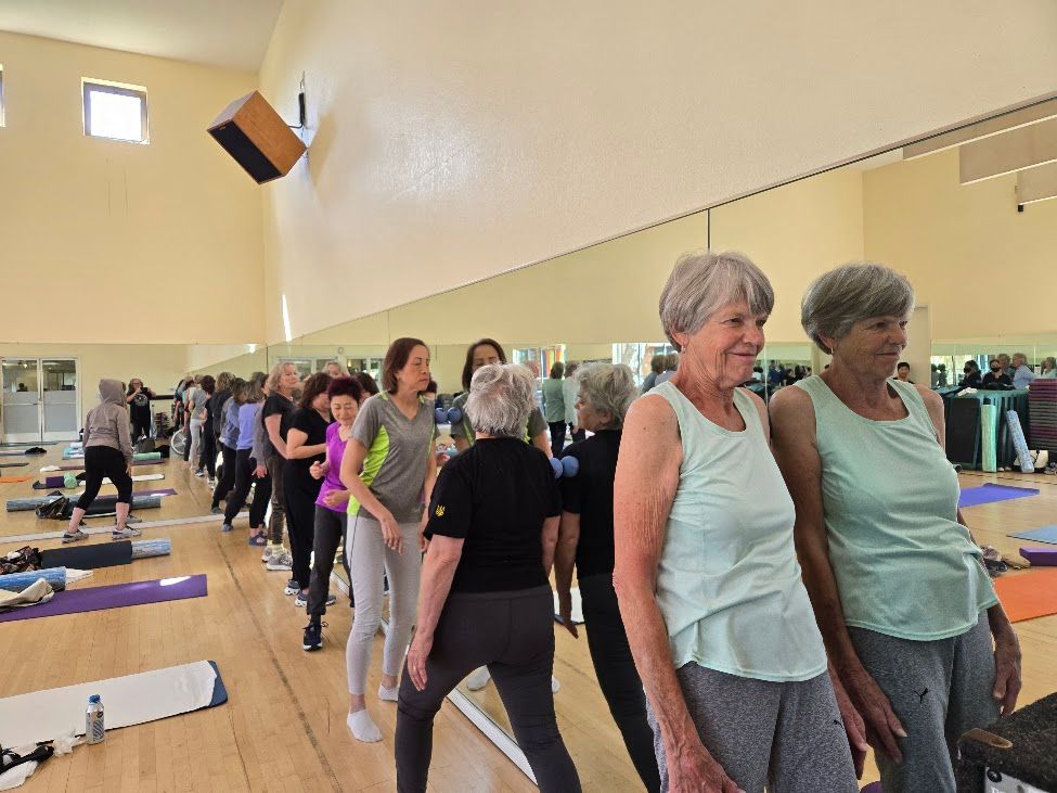 People exercising in a mirrored studio, with yoga mats and a large suspended speaker.
