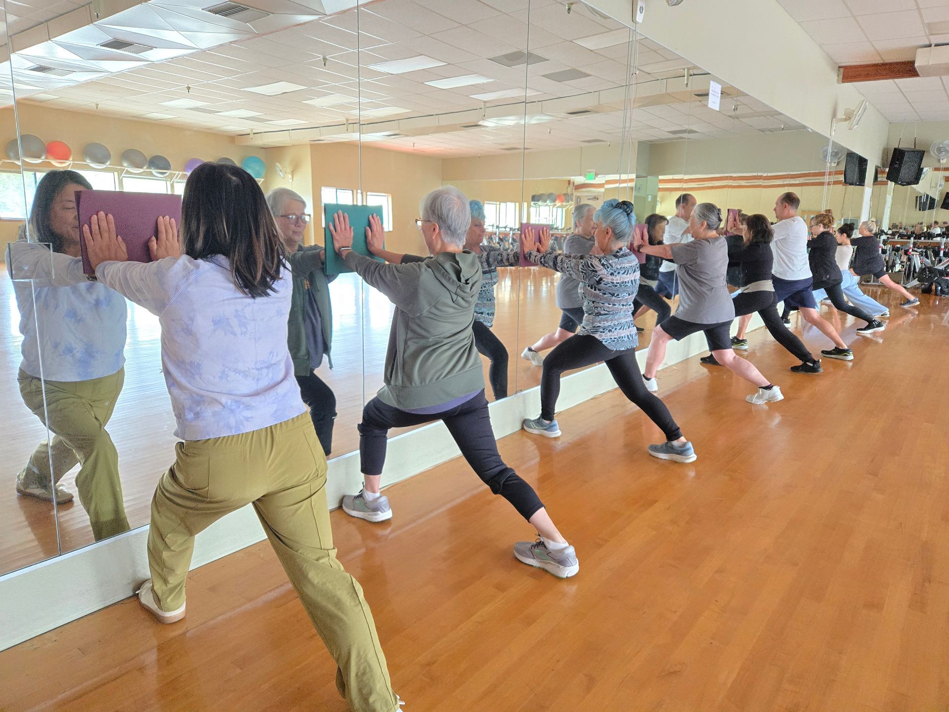 Group fitness class doing synchronized lunges in a mirrored studio with wooden floors
