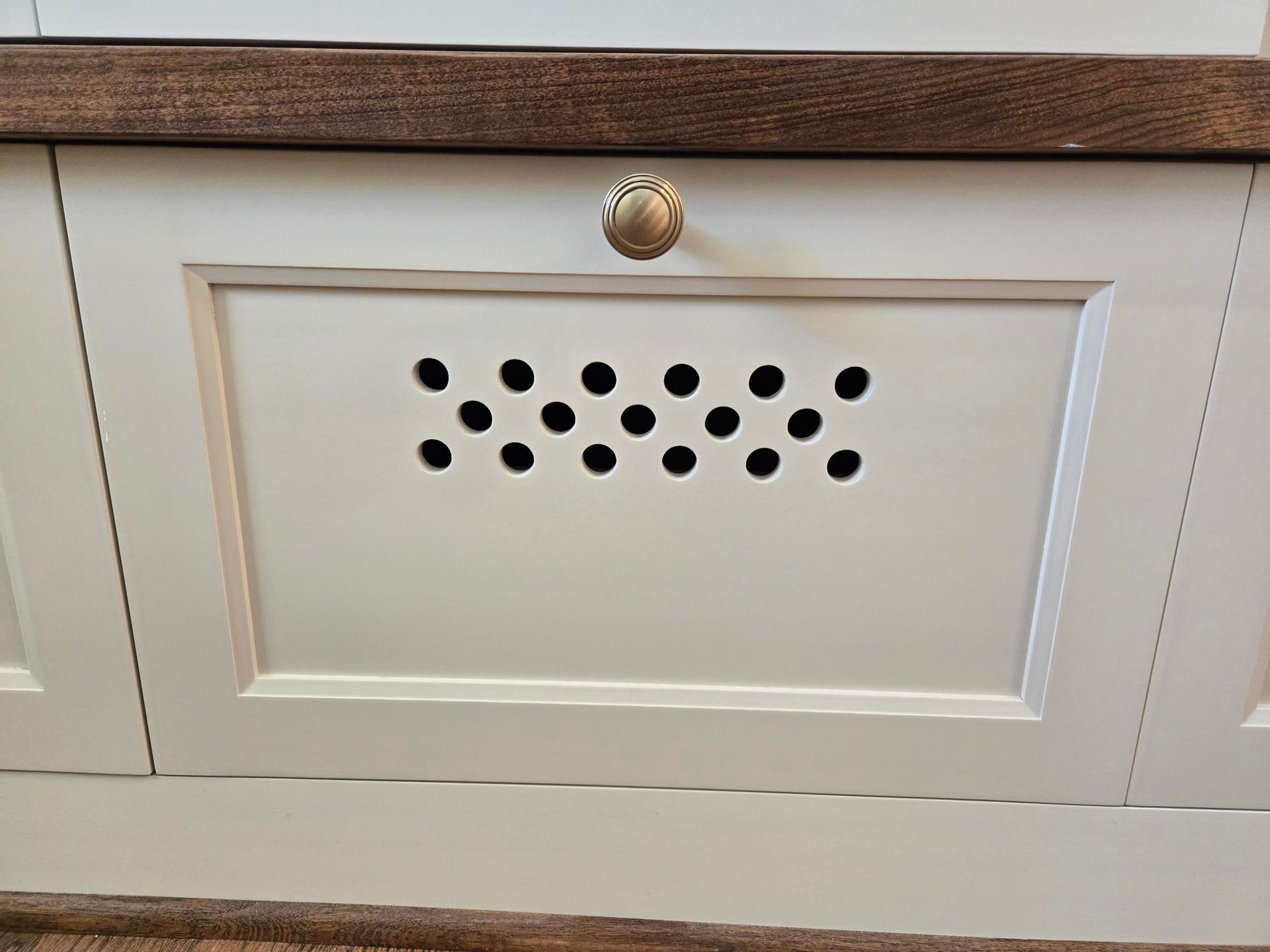 White cabinet door with a brass knob and a perforated black vent panel.