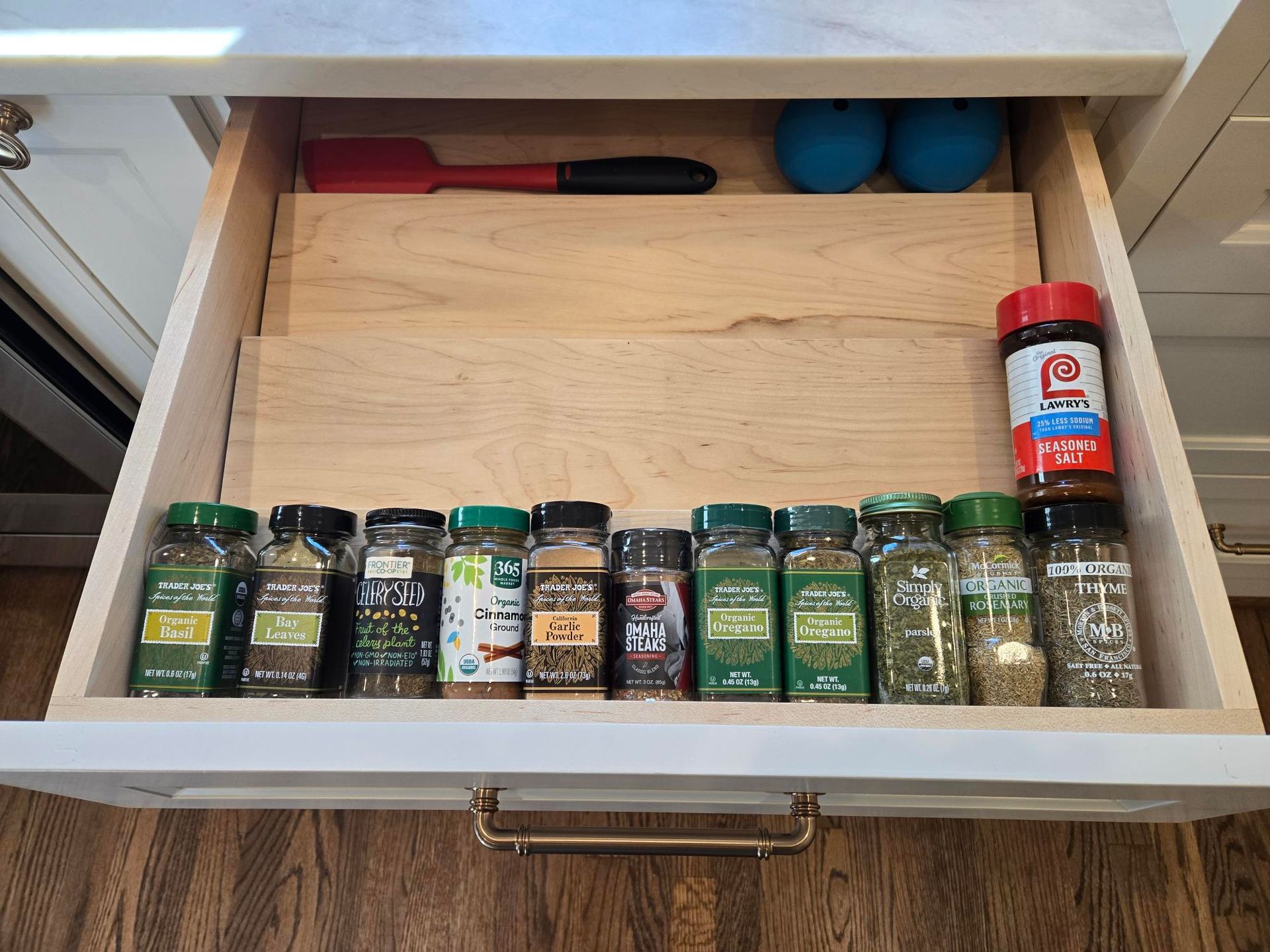 Open kitchen drawer with spice jars lined up in front of a wooden cutting board.