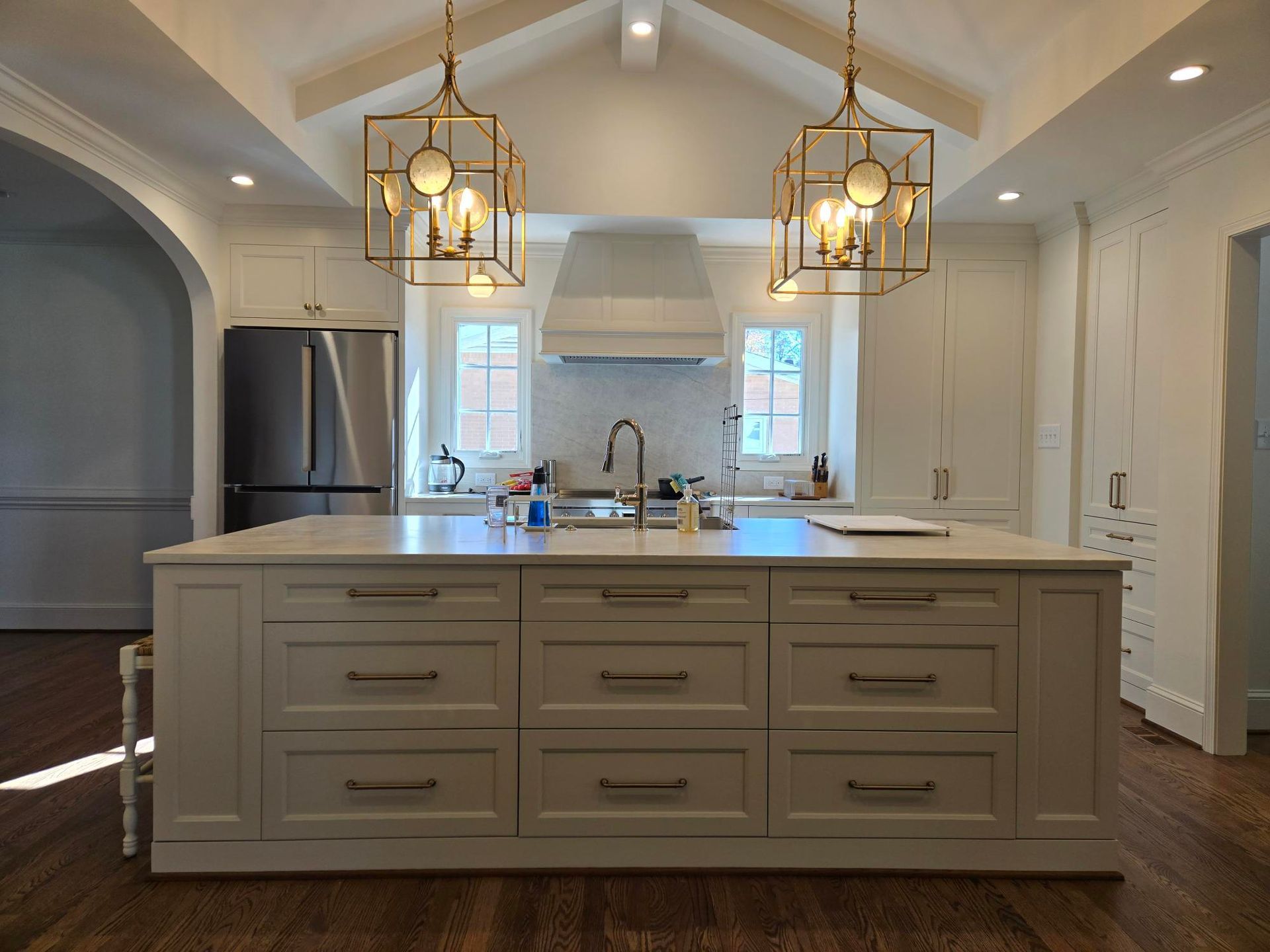Modern white kitchen with a large island, pendant lights, stainless fridge, and vaulted ceiling.