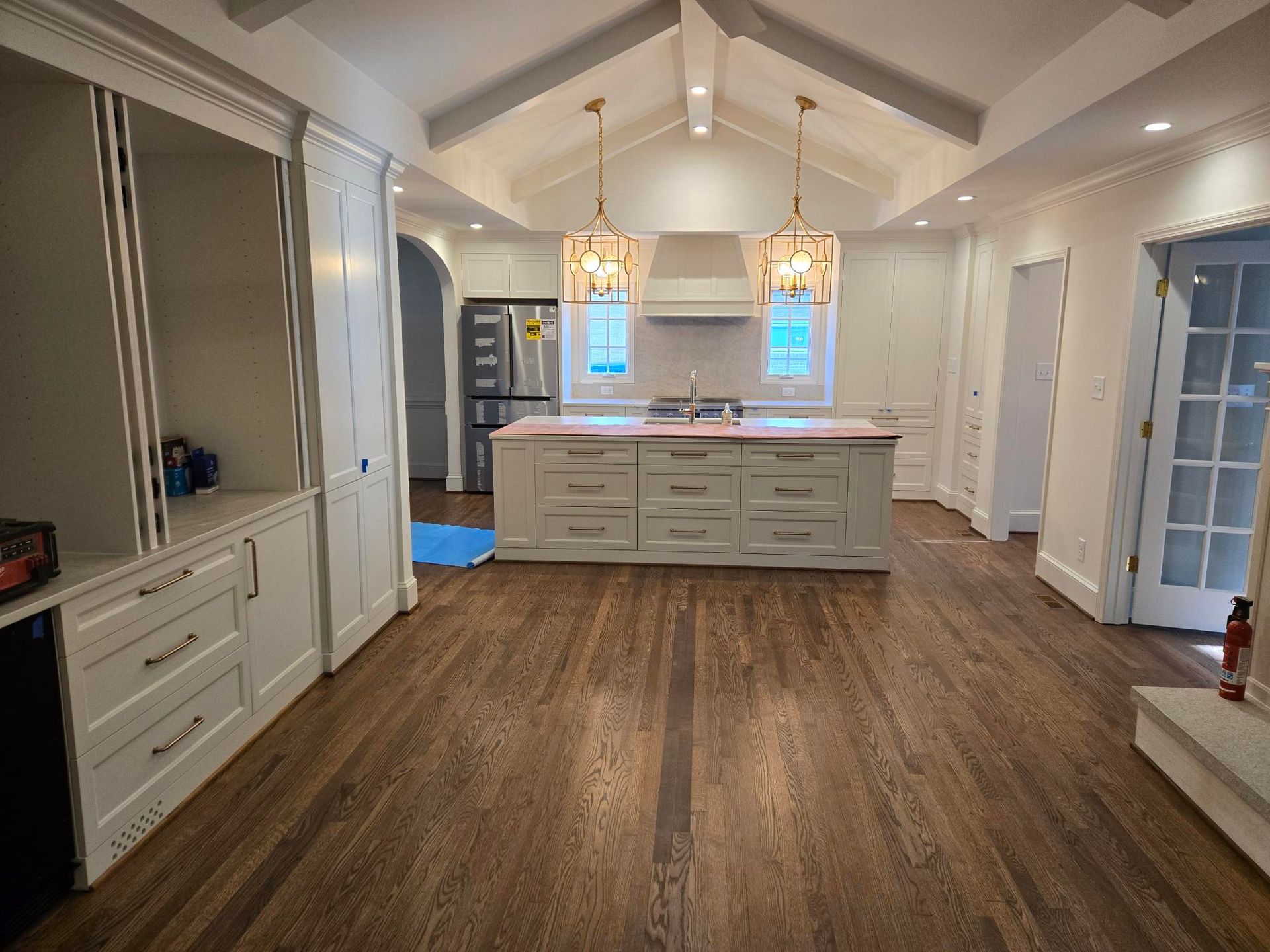 Spacious white kitchen with wood floors, central island, pendant lights, and vaulted ceiling.