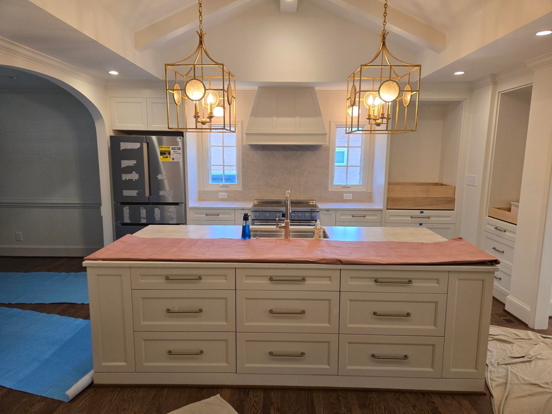 Bright kitchen with cream cabinets, pink island, stainless fridge, and two brass pendant lights