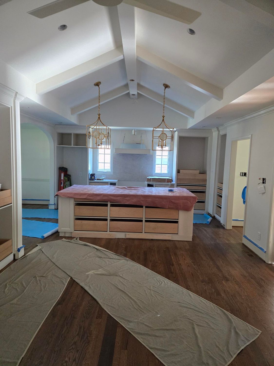 Bright living room under renovation with exposed beams, wrapped furniture, and protective floor covering