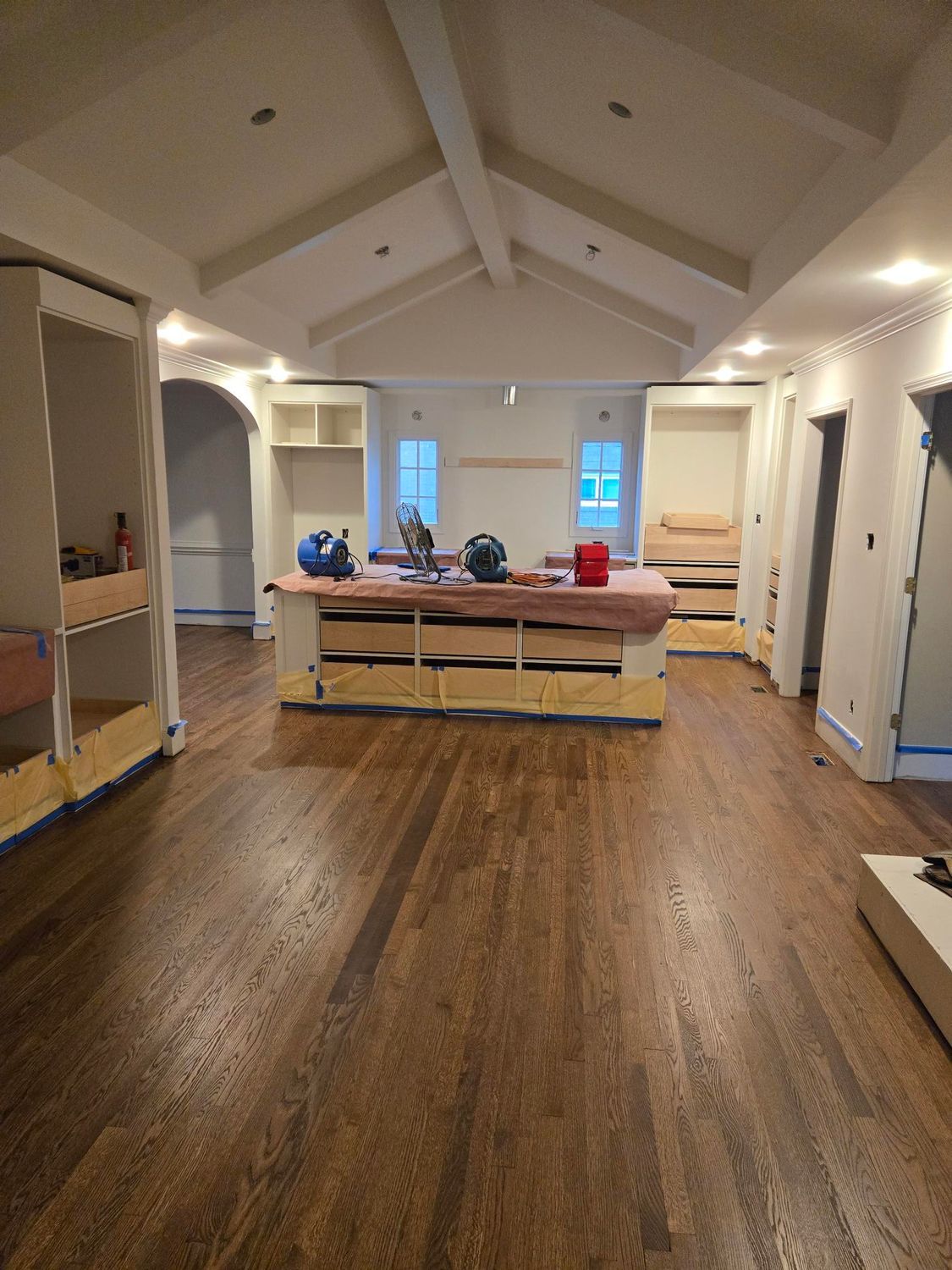 Empty living room with vaulted ceiling, wood floors, and a sofa facing two windows.
