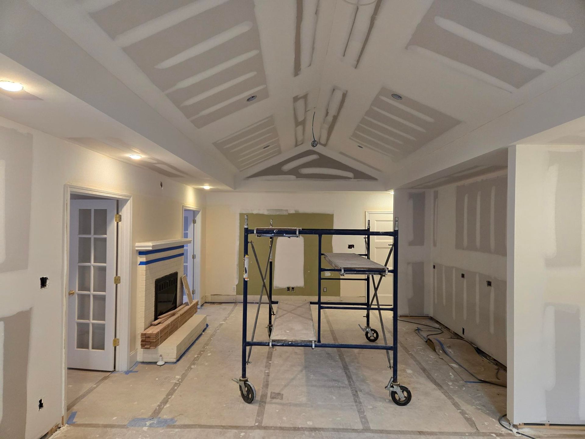 Renovation room with white vaulted ceiling, scaffolding, and unfinished walls and floors