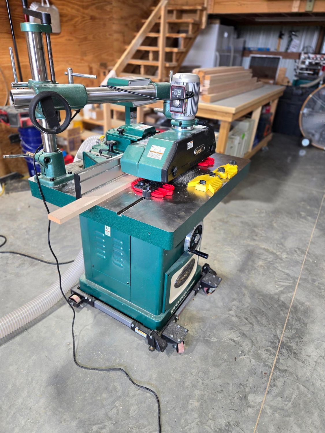 Green woodworking machine in a workshop, with a fence, red knobs, and a saw table on wheels.
