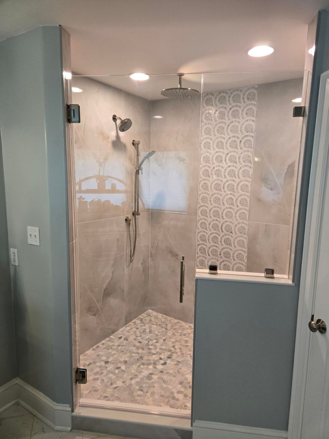 Walk-in shower with gray tile walls, pebble floor, and chrome fixtures in a bathroom.
