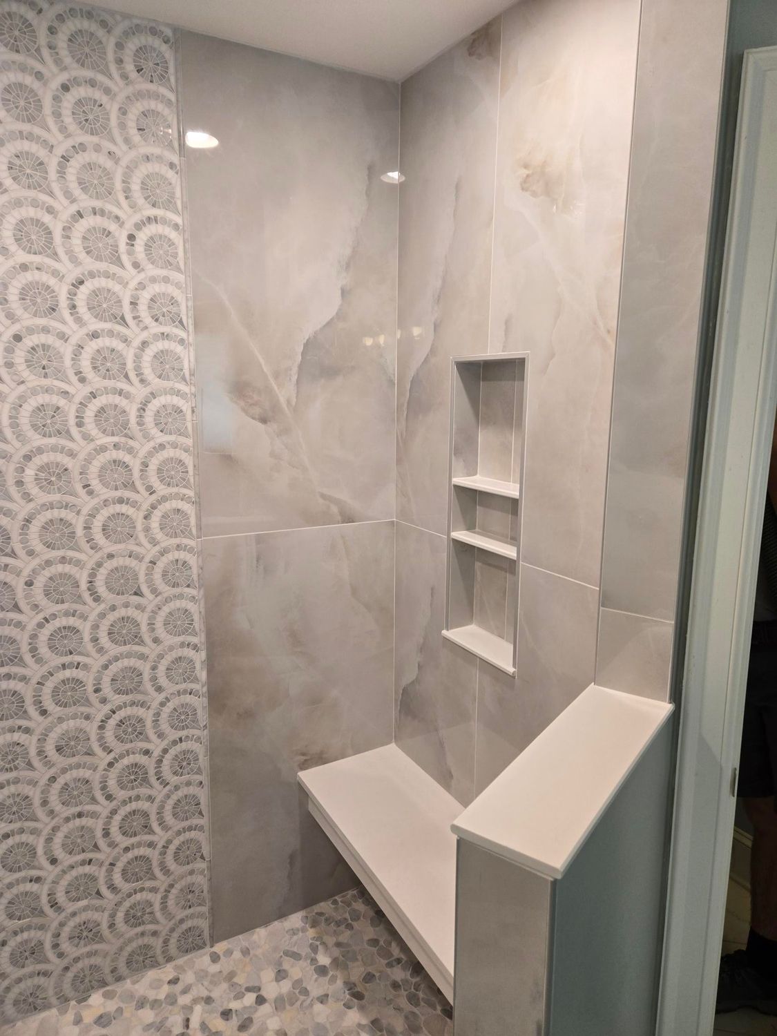 Modern tiled shower with built-in corner bench, recessed shelves, and patterned accent wall.
