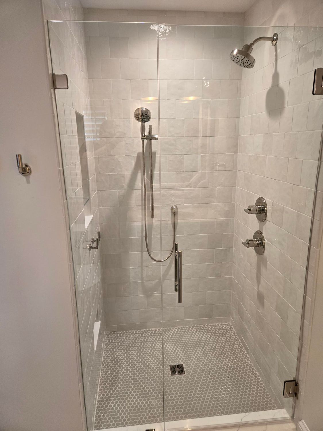 Accessible walk-in shower with white tile walls, gray floor, grab bars, and a handheld showerhead.