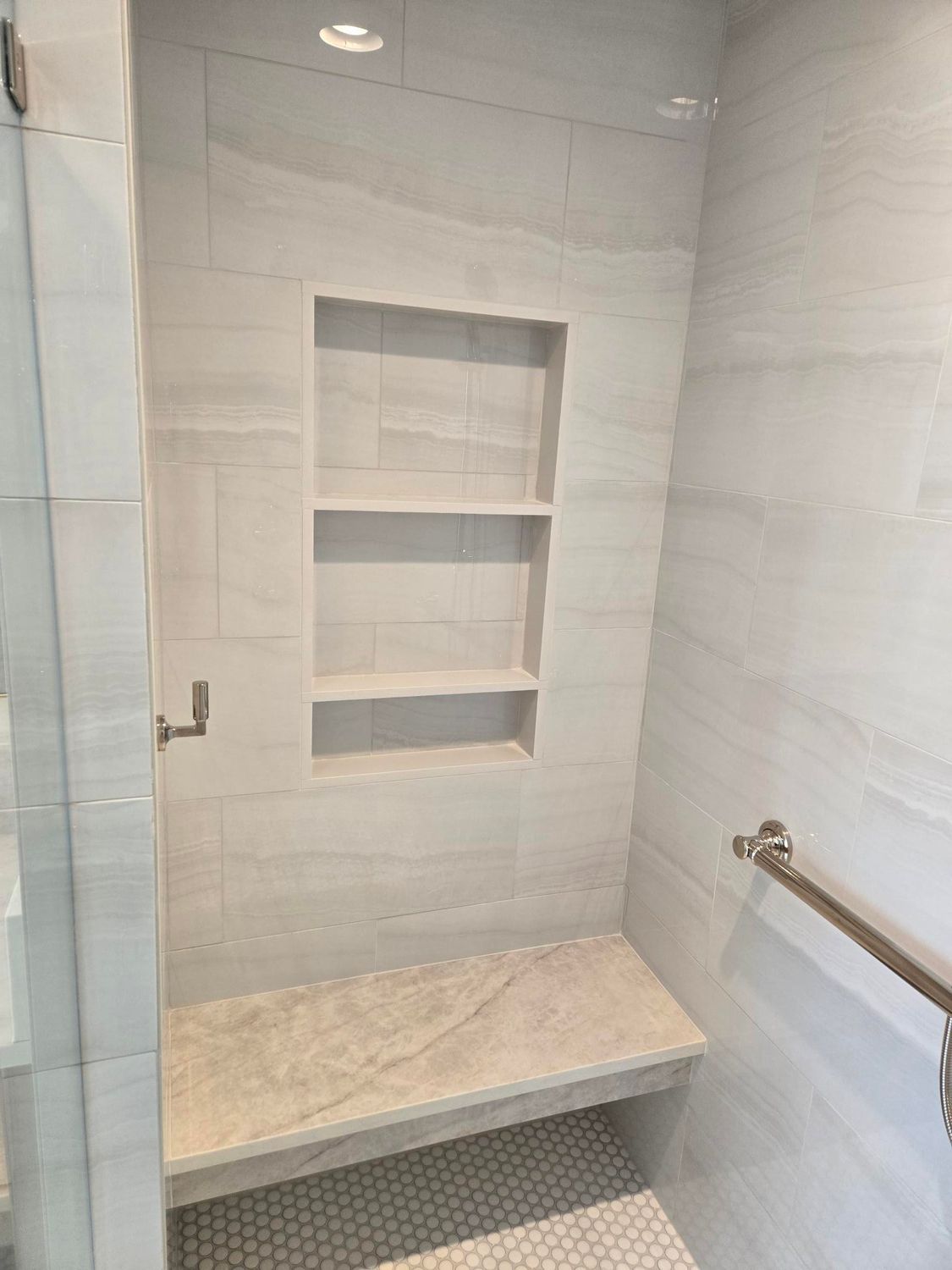 Bathroom shower with recessed shelves, marble bench, and grab bar.