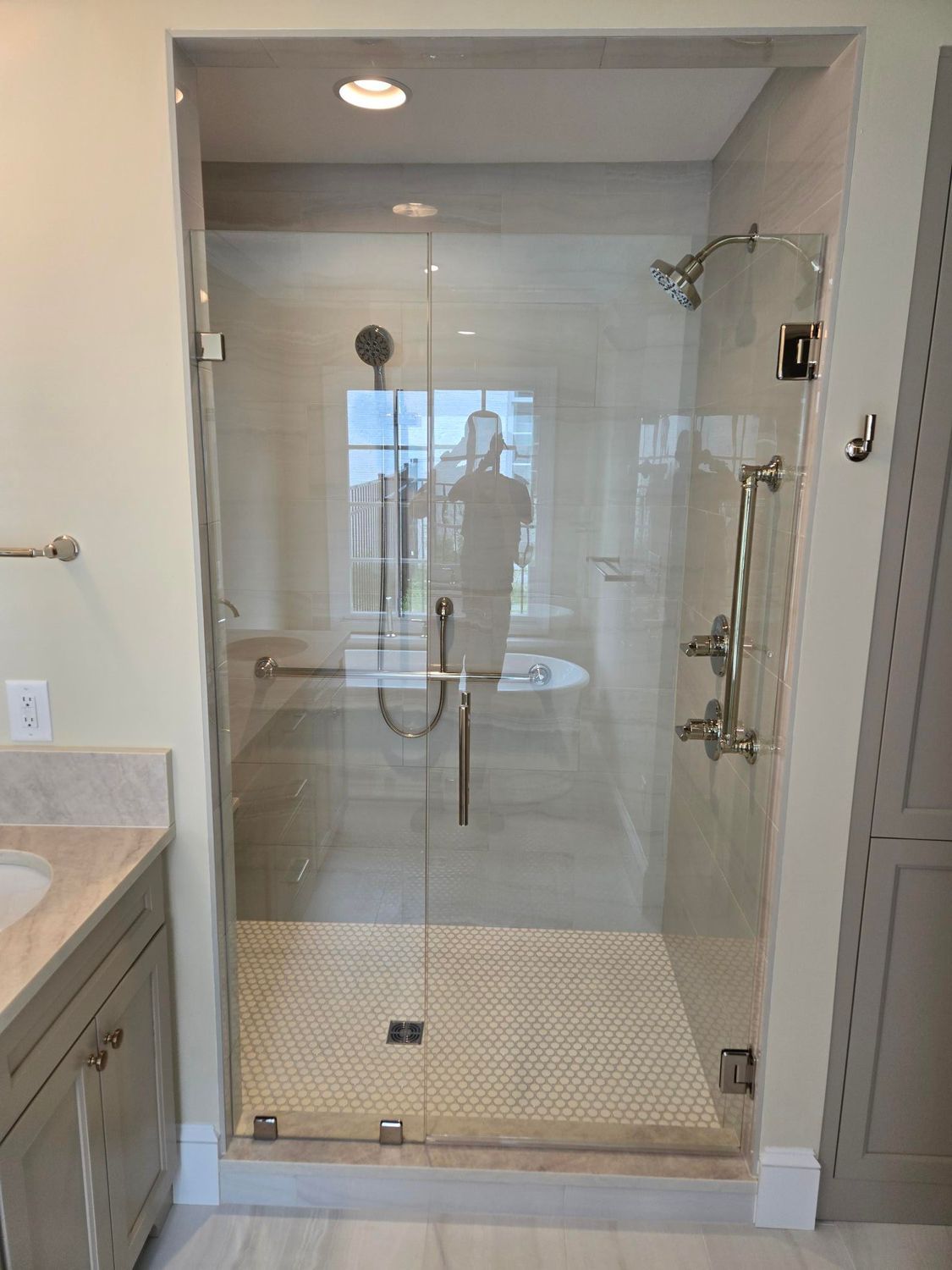 Glass walk-in shower with tiled floor, rainfall head, handheld wand, and clear doors in a bathroom