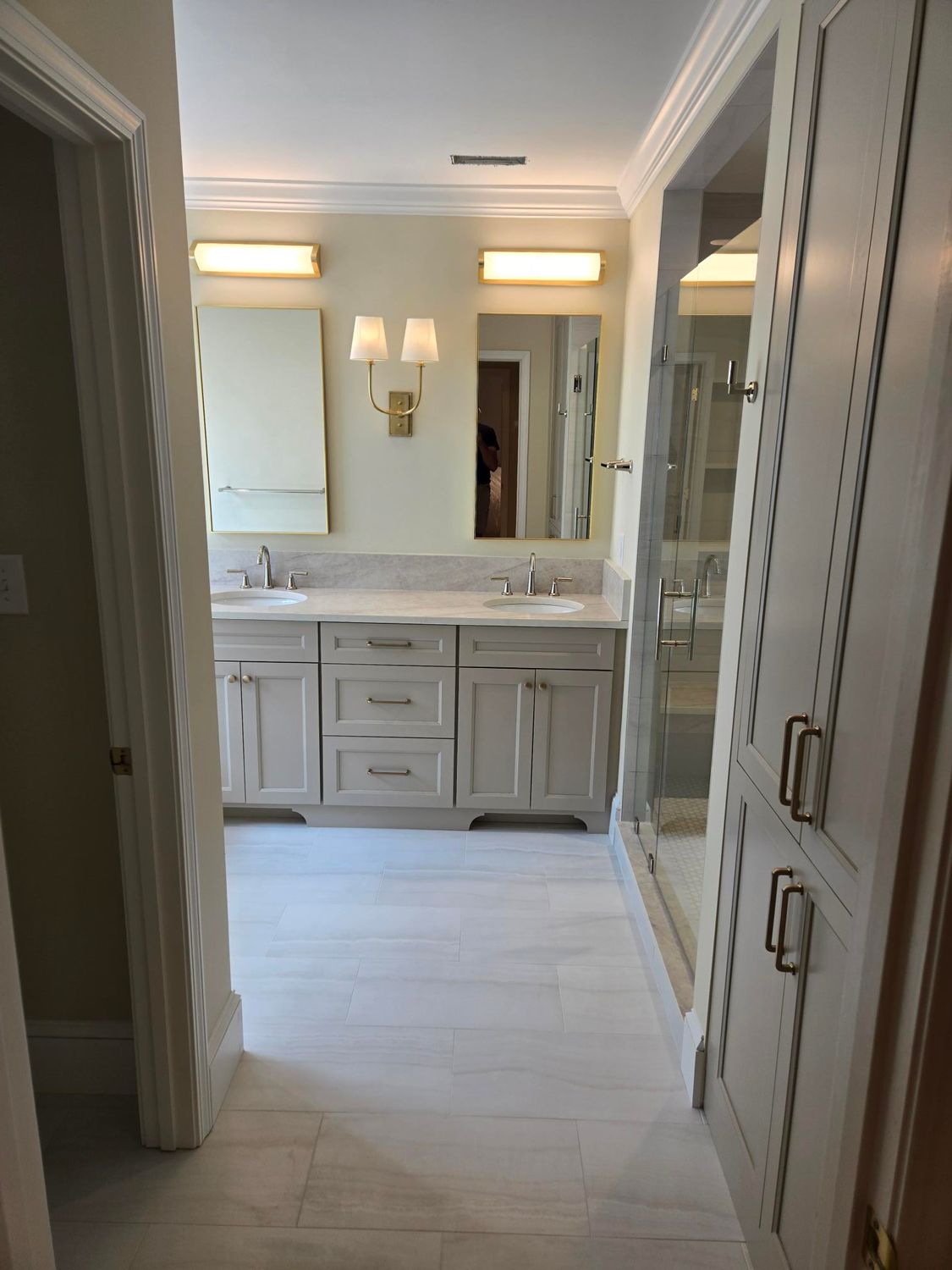 Bright bathroom vanity with mirror, twin sconces, and open doorway in a narrow hallway