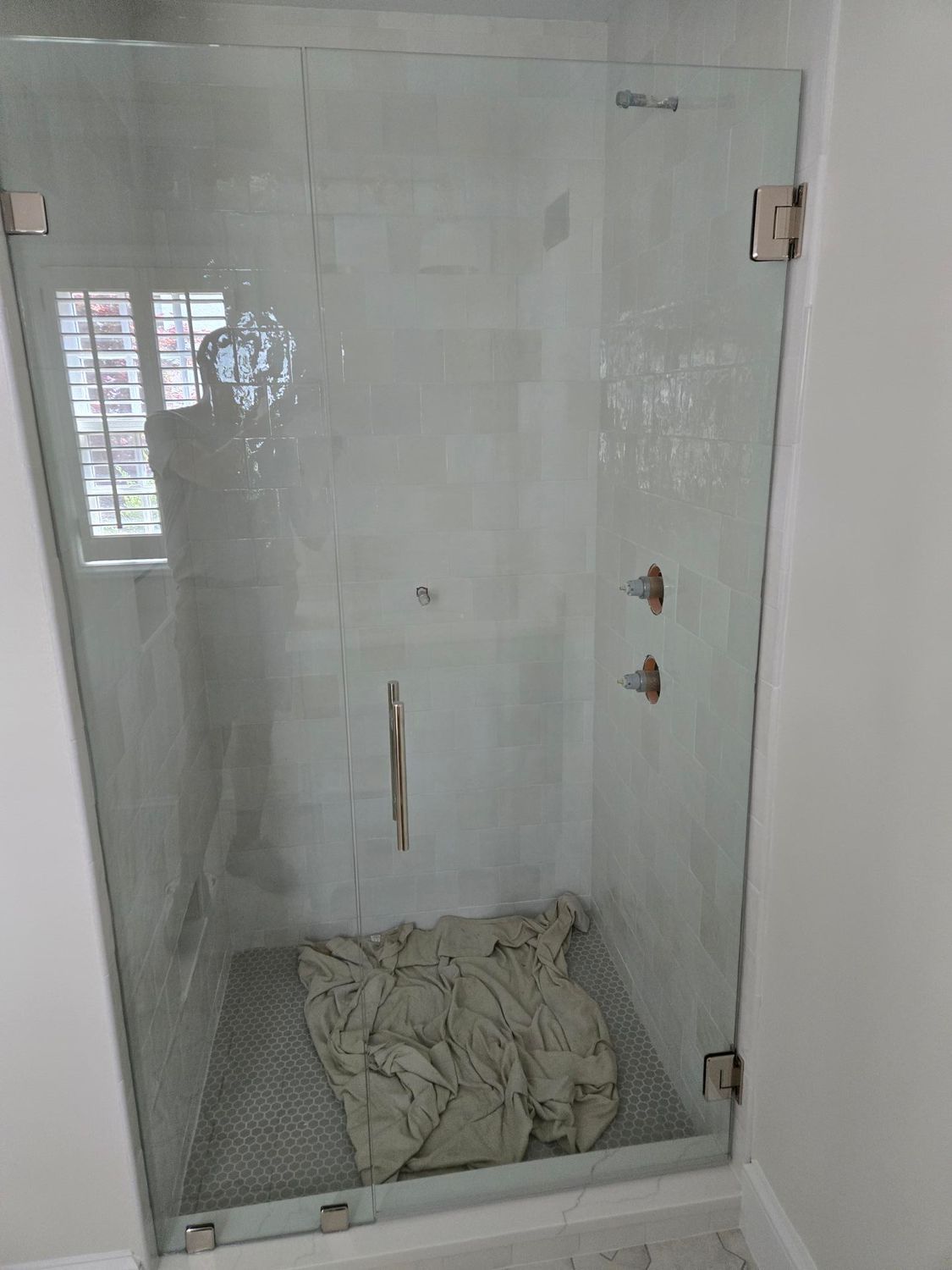 Small tiled shower stall with a folded cloth or tarp on the floor and a glass door.