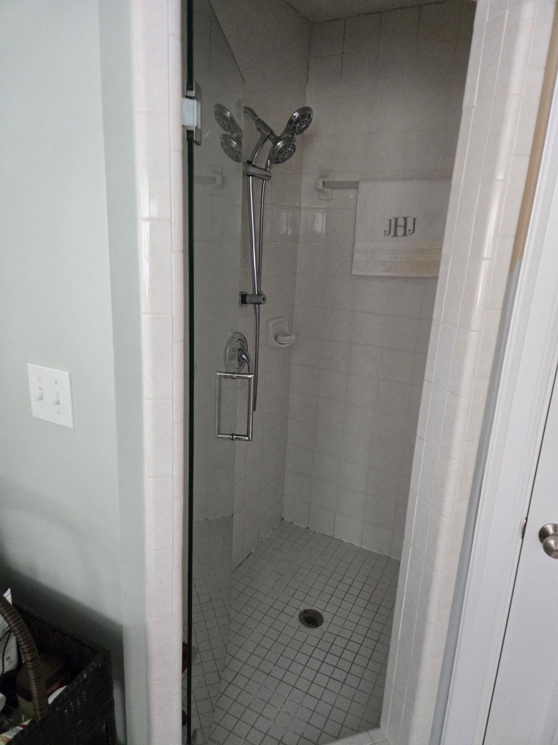 Small tiled walk-in shower with chrome handheld showerhead and wall grab bars.