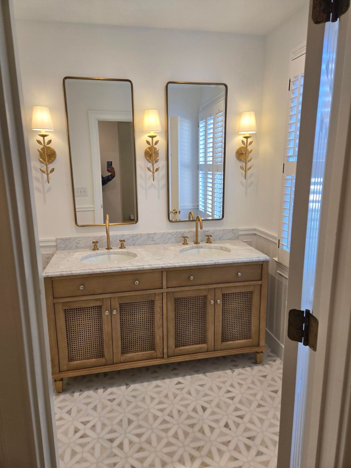 Elegant bathroom vanity with two mirrors, brass sconces, and woven wood cabinet doors in a bright white room