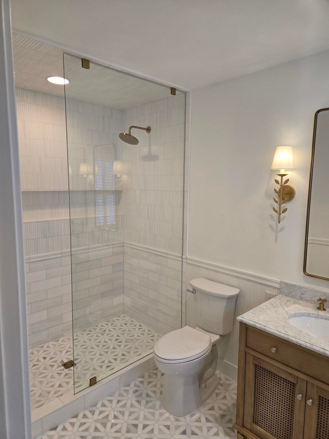 Bright modern bathroom with glass shower, white tiled walls, toilet, and wooden vanity with marble top