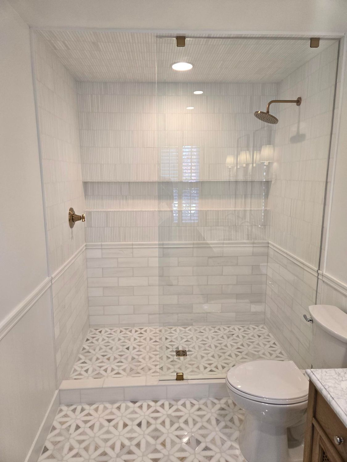 Small white tiled walk-in shower with built-in shelves, rain showerhead, and toilet beside it