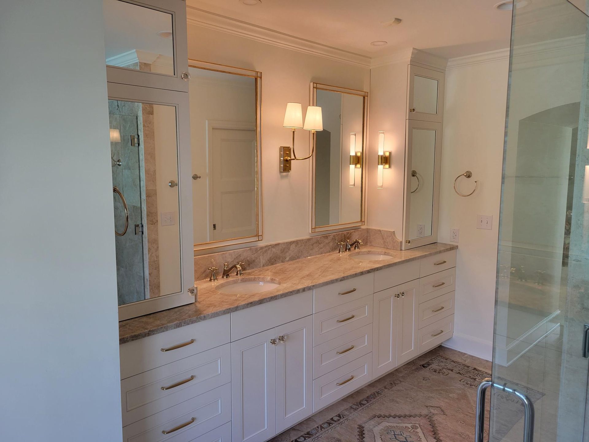 Elegant bathroom vanity with double sinks, mirrors, sconces, and glass shower enclosure