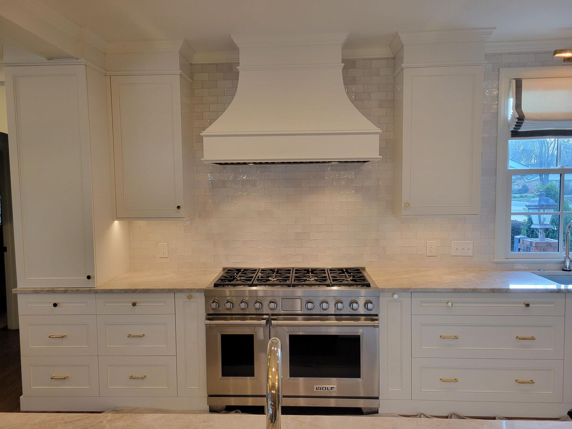Bright white kitchen with marble countertops, stainless range, and a large vent hood.