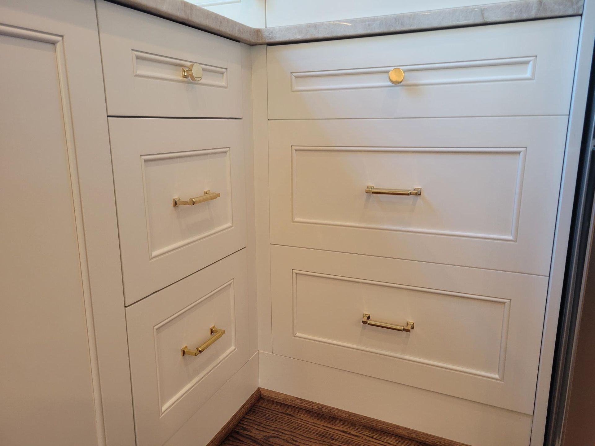 White built-in cabinets with brass handles in a corner alcove beneath a window shelf