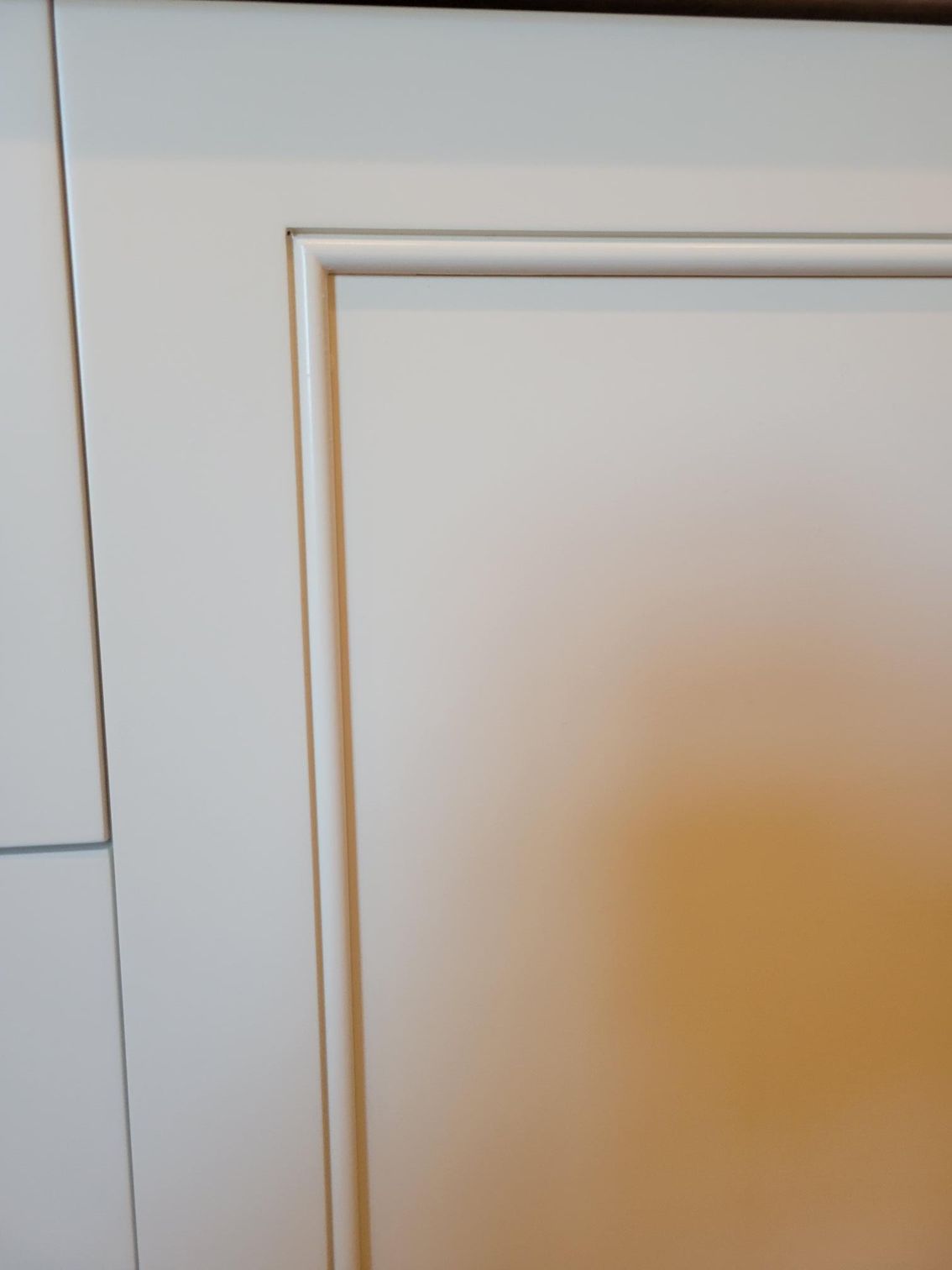 White paneled cabinet door with gold trim and a faint orange stain on the lower right.