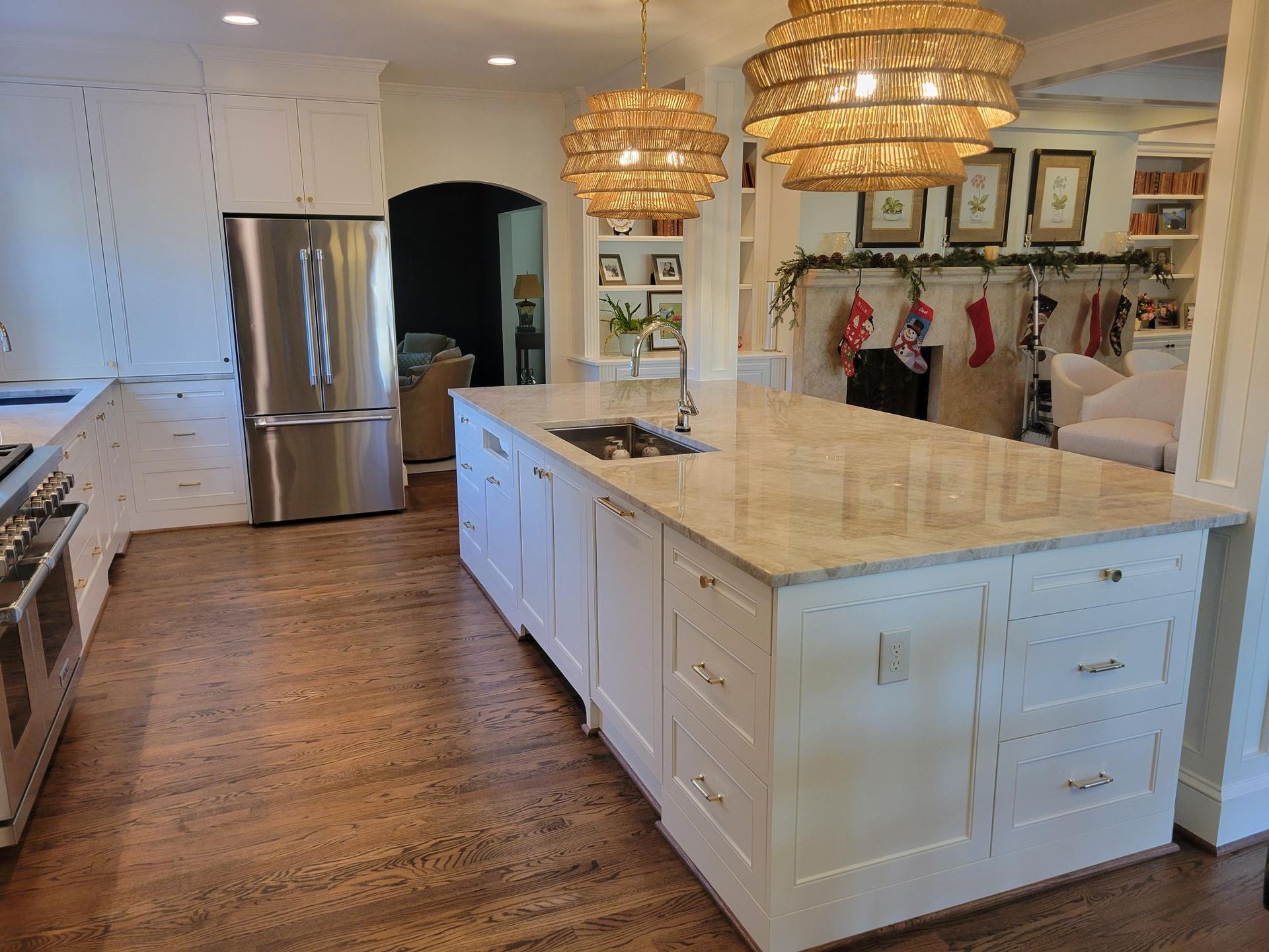 Bright white kitchen with large marble island, pendant lights, stainless fridge, and hardwood floors