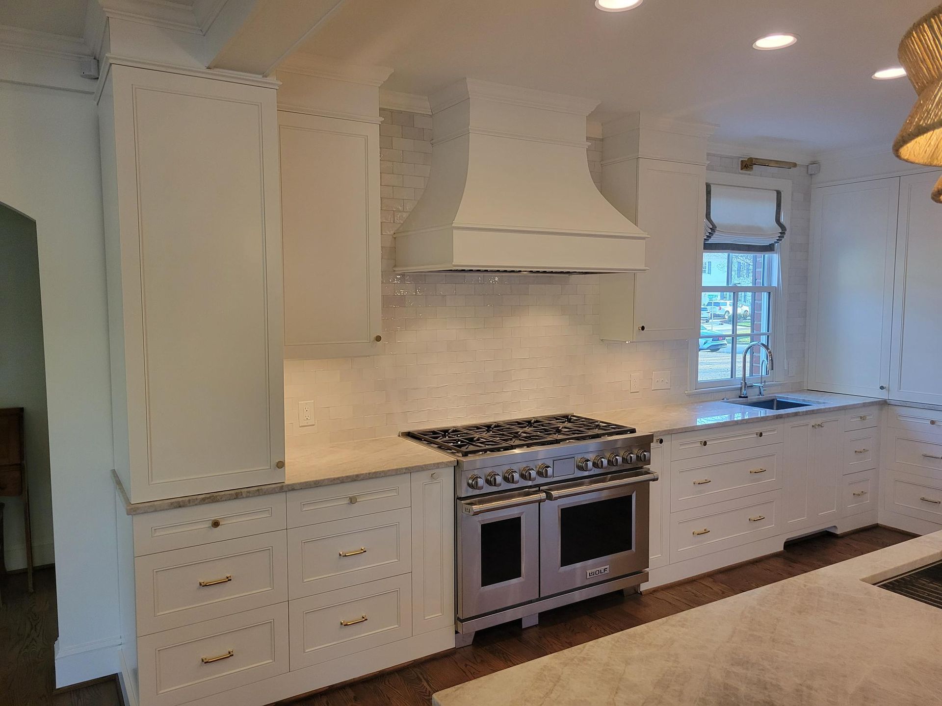 Bright white kitchen with cabinets, island, stainless stove, and patterned tile floor.