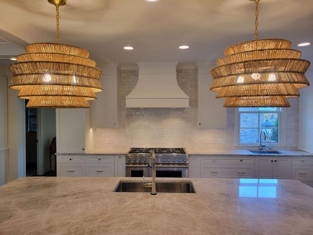Bright modern kitchen with marble island, white cabinets, stove, and two woven pendant lights