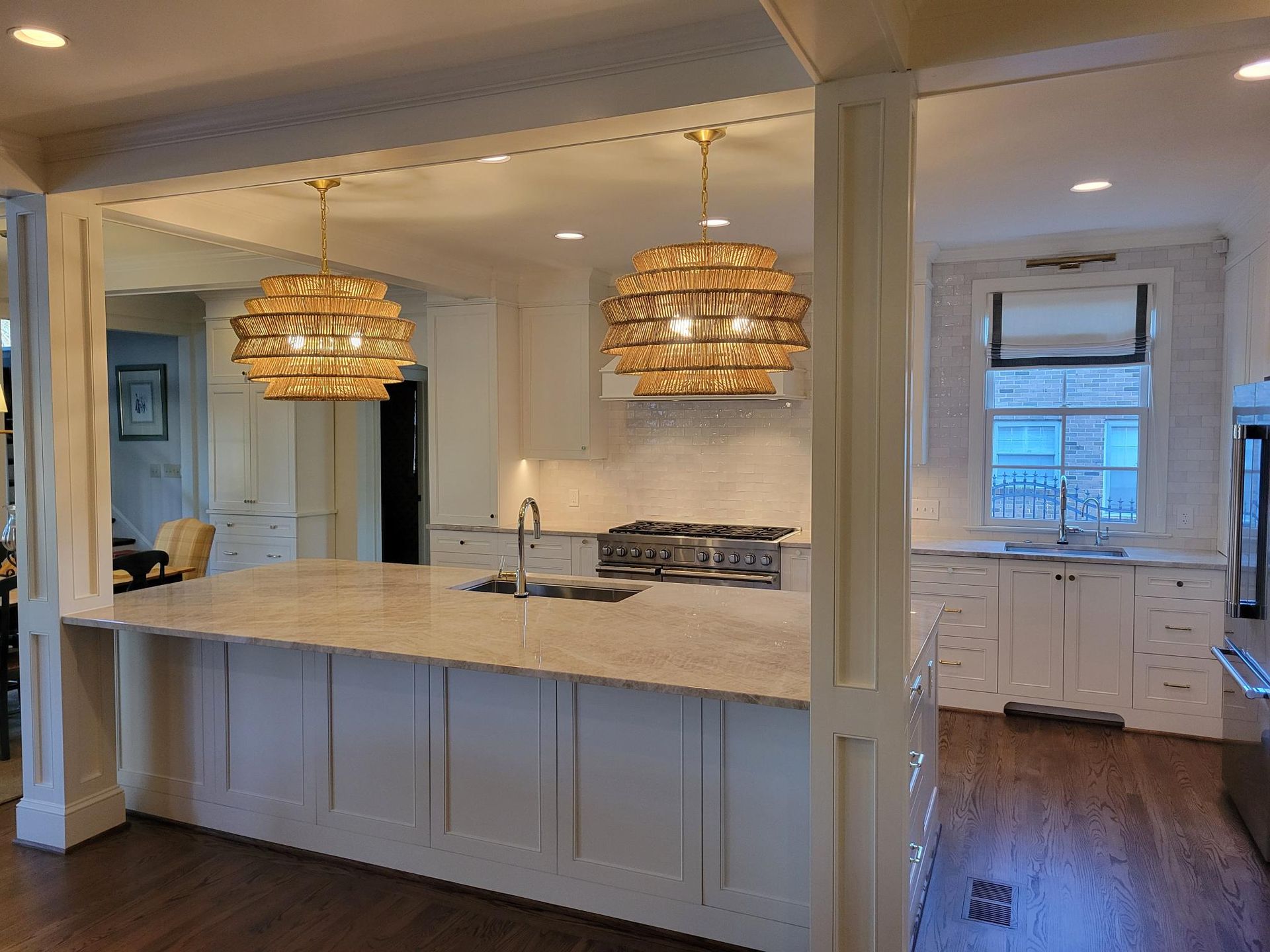 Bright white kitchen with large island, woven pendant lights, and wood floors