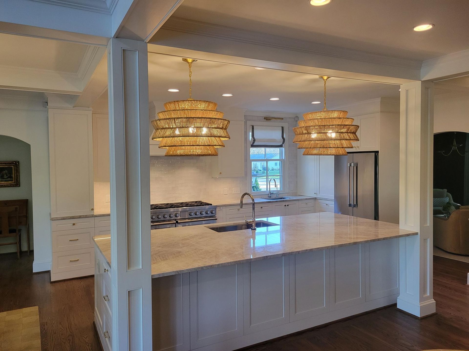 Bright kitchen with large island, white cabinetry, and two woven pendant lights under recessed ceiling lights