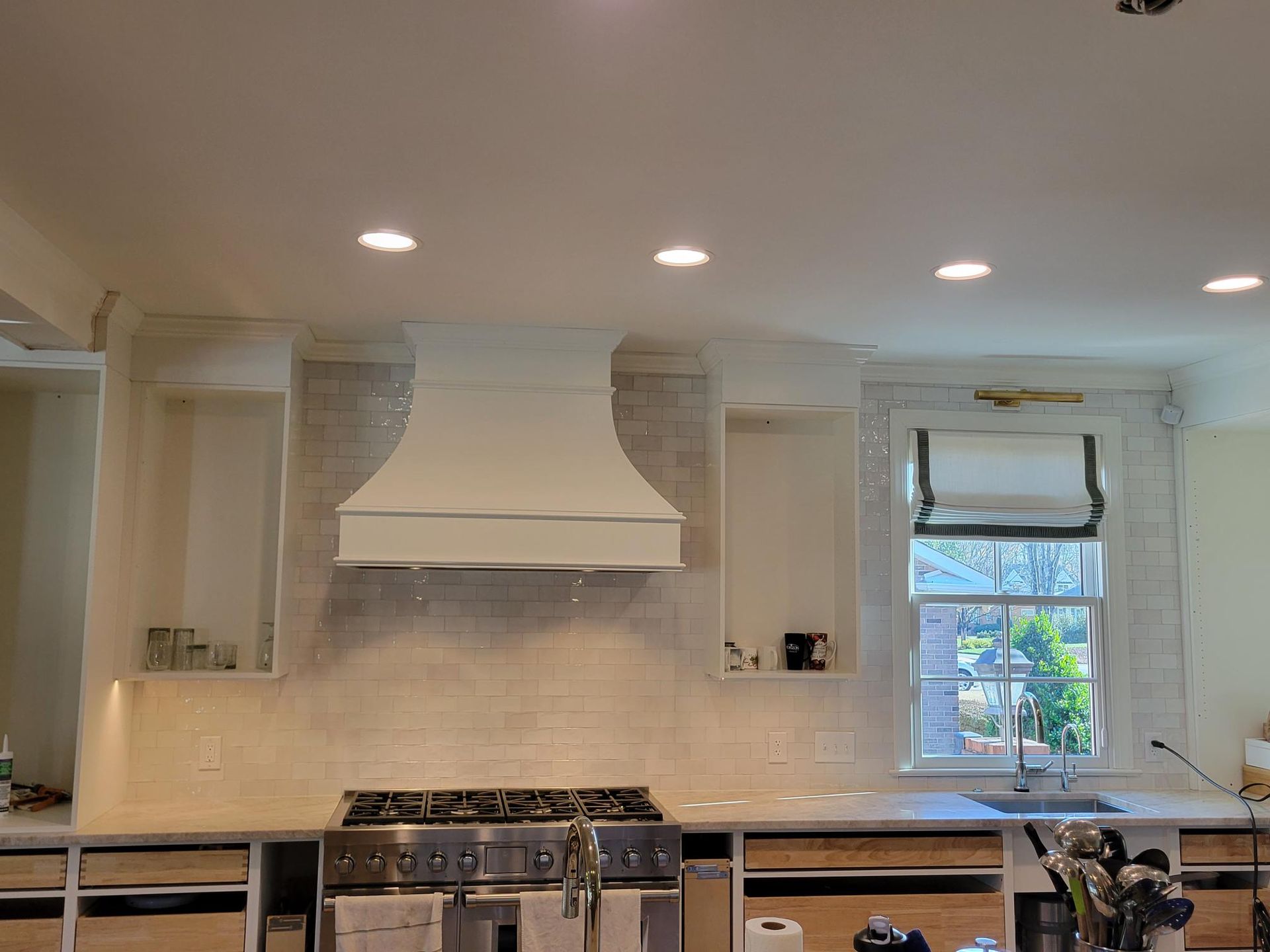Bright white kitchen with stainless stove, hood, recessed lights, and a window over the sink