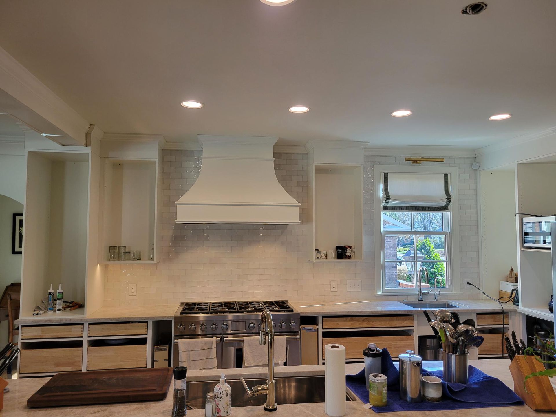 Modern kitchen with white cabinets, large stove, island, and stainless hood under recessed lights