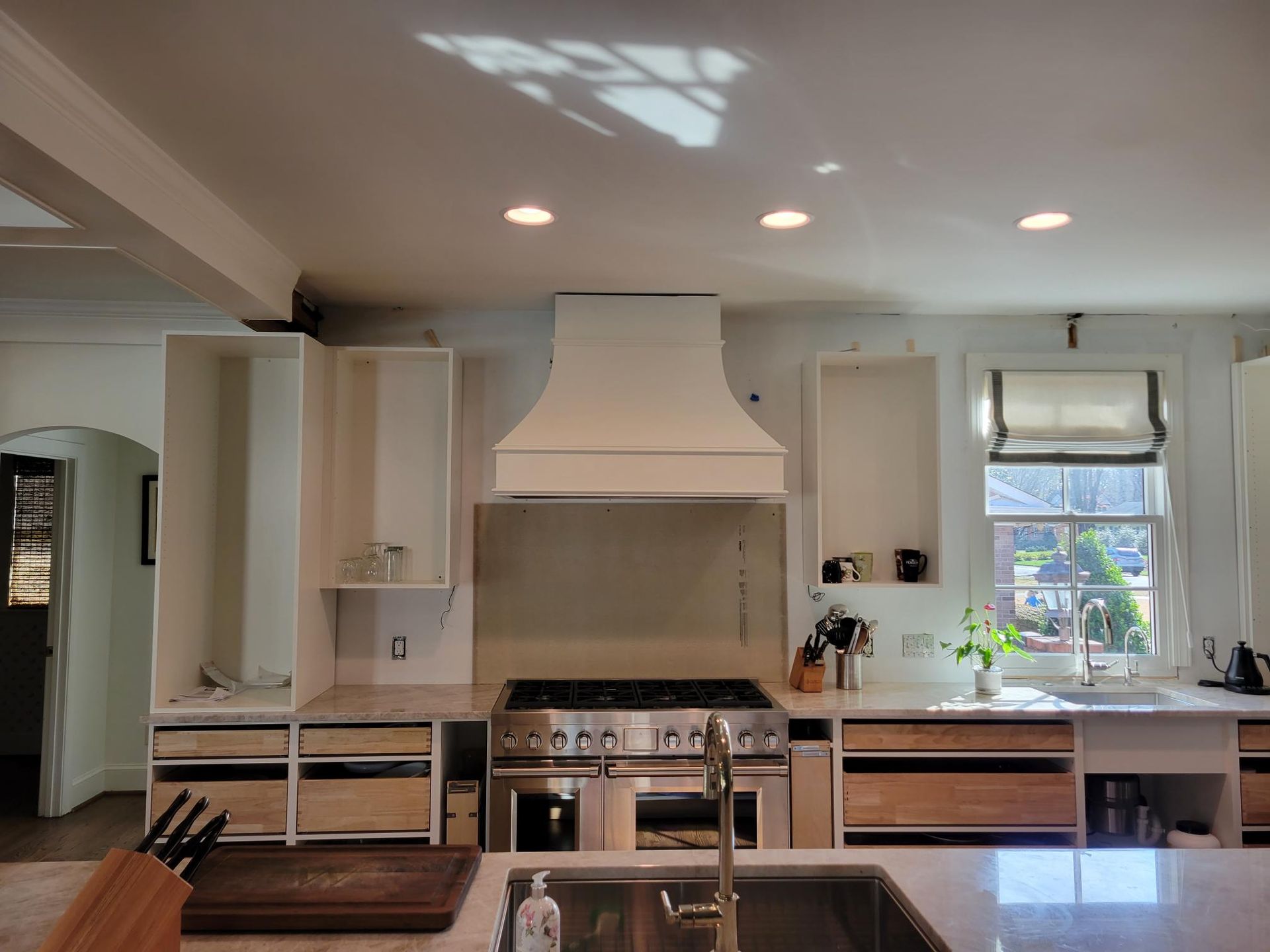 Modern kitchen with white cabinets, central range hood, wood island, and a bright window over the sink