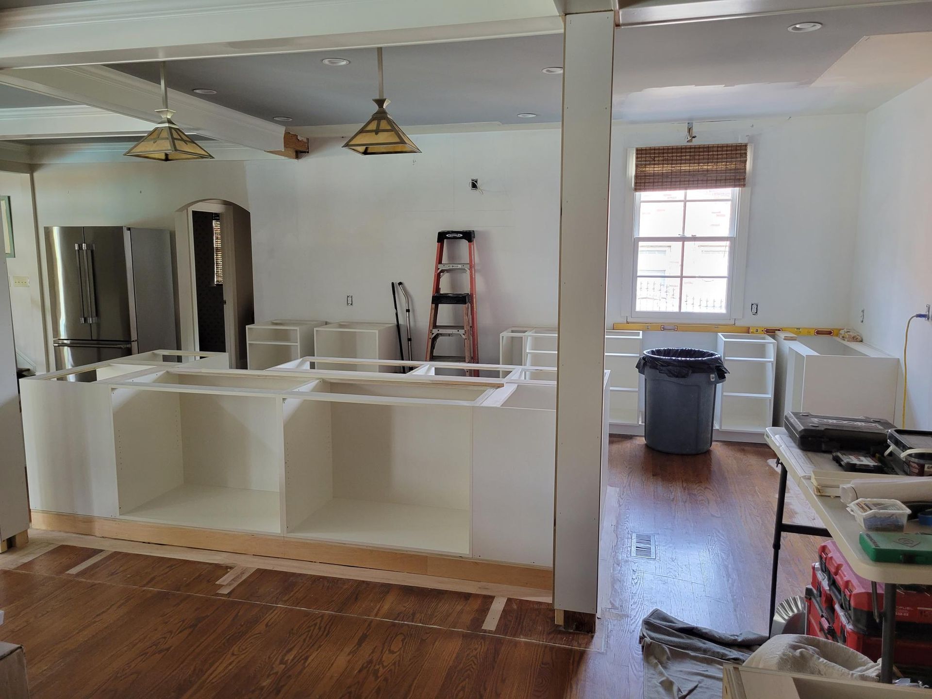 Partially renovated kitchen with white cabinets, wood floors, ladder, and construction materials