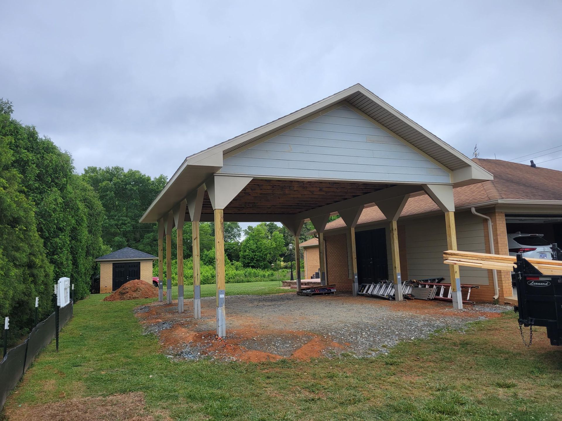 Partially built house with a covered porch, wooden framing, and construction materials on a muddy lot under cloudy skies