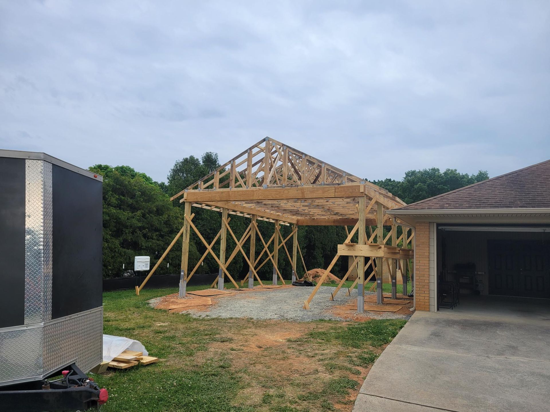 Wooden house frame under construction beside a brick garage on a cloudy day