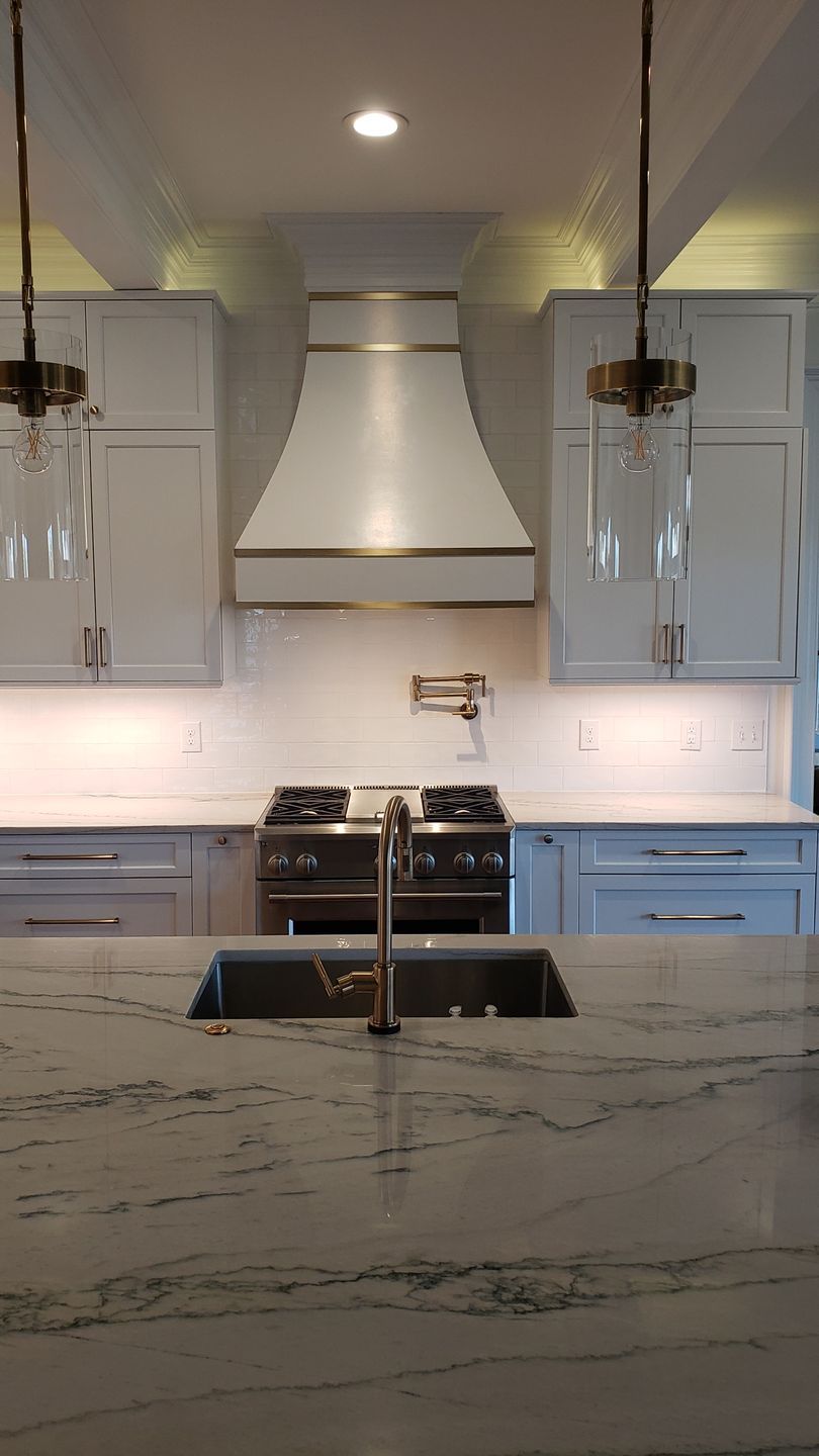 Modern kitchen with marble island, farmhouse sink, stainless range hood, and pendant lights