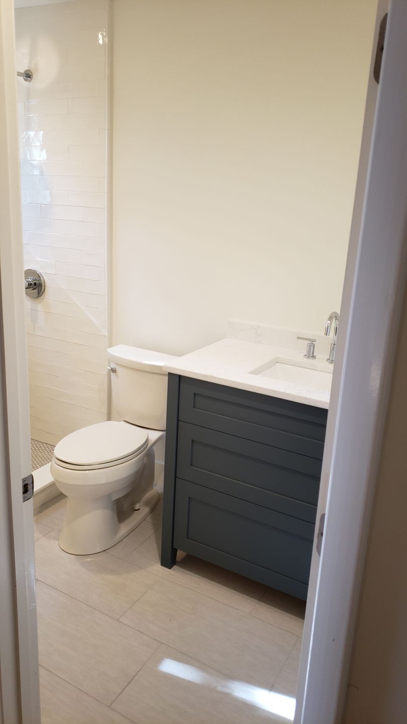 Small bathroom with white toilet, vanity sink, and beige tile floor.