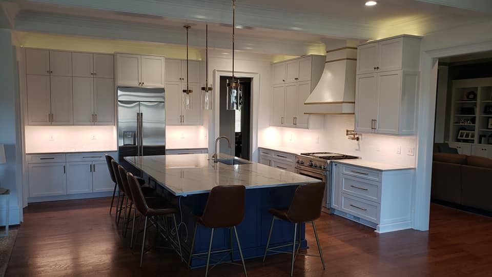 Modern white kitchen with a large island, pendant lights, and dark barstools on a wood floor