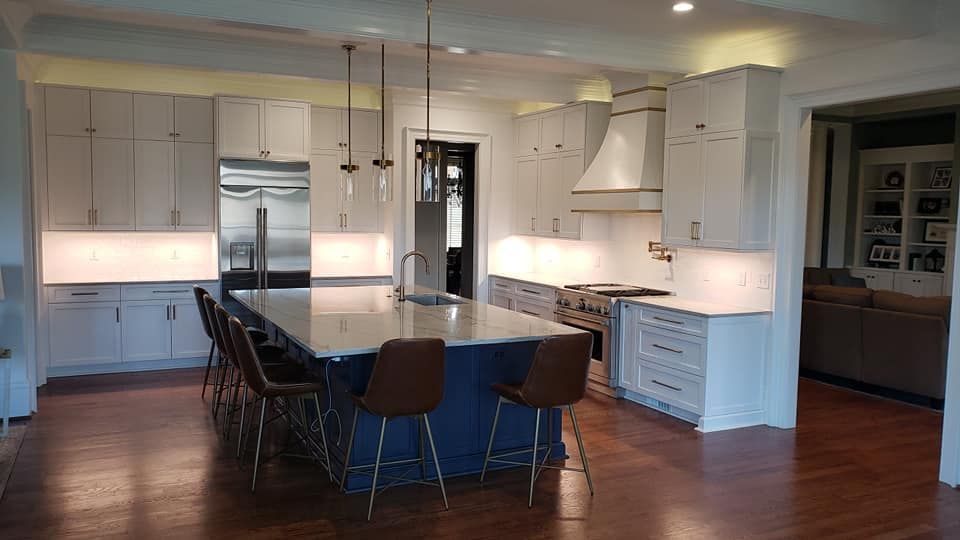 Modern white kitchen with island, pendant lights, dark stools, and hardwood floors