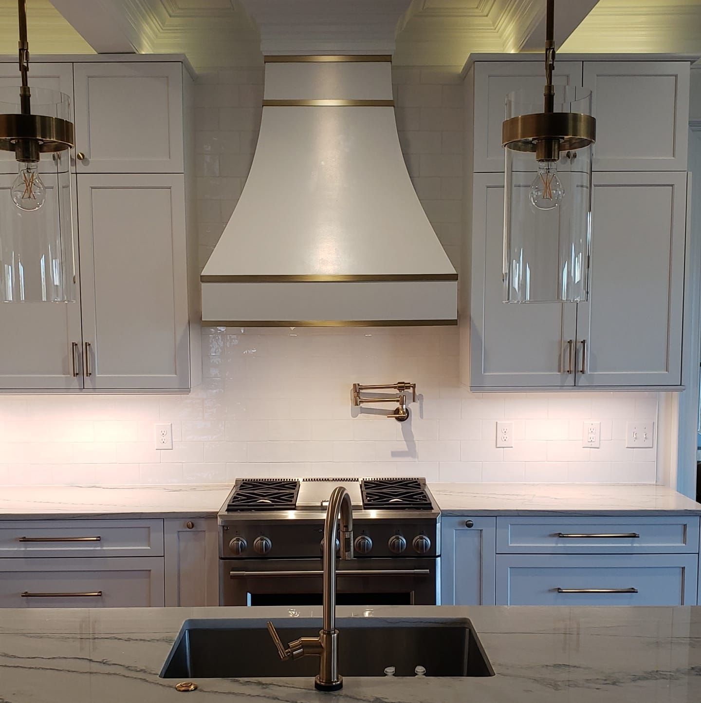 Modern kitchen with white cabinets, gray island countertop, stainless stove, and central sink faucet