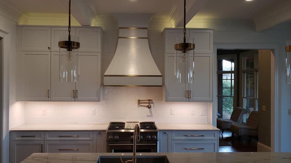 Modern kitchen with white cabinets, stainless range hood, and pendant lights over a central island