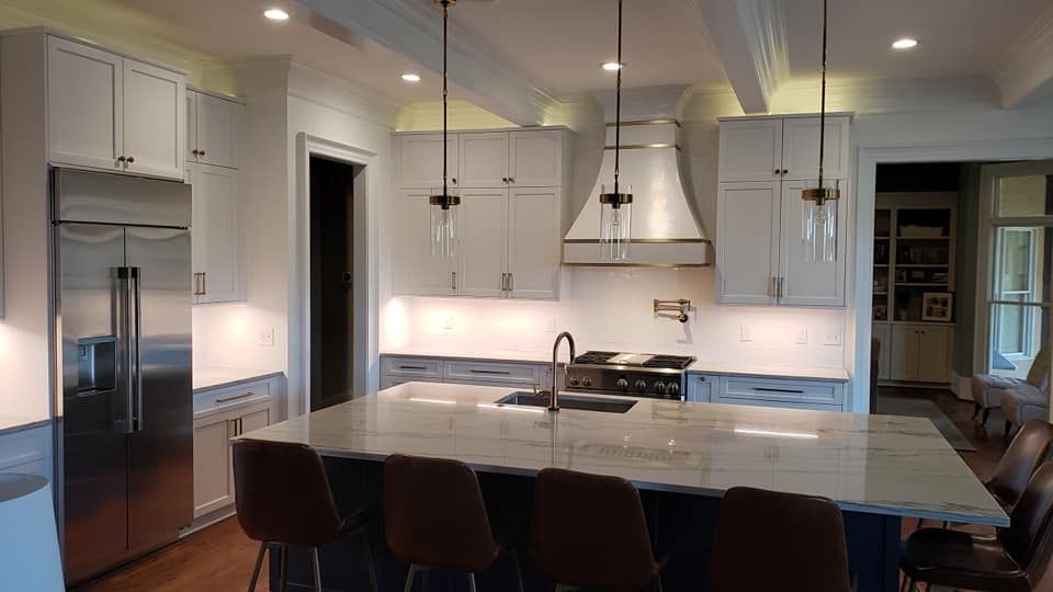 Modern white kitchen with stainless steel appliances, island, pendant lights, and dark barstools