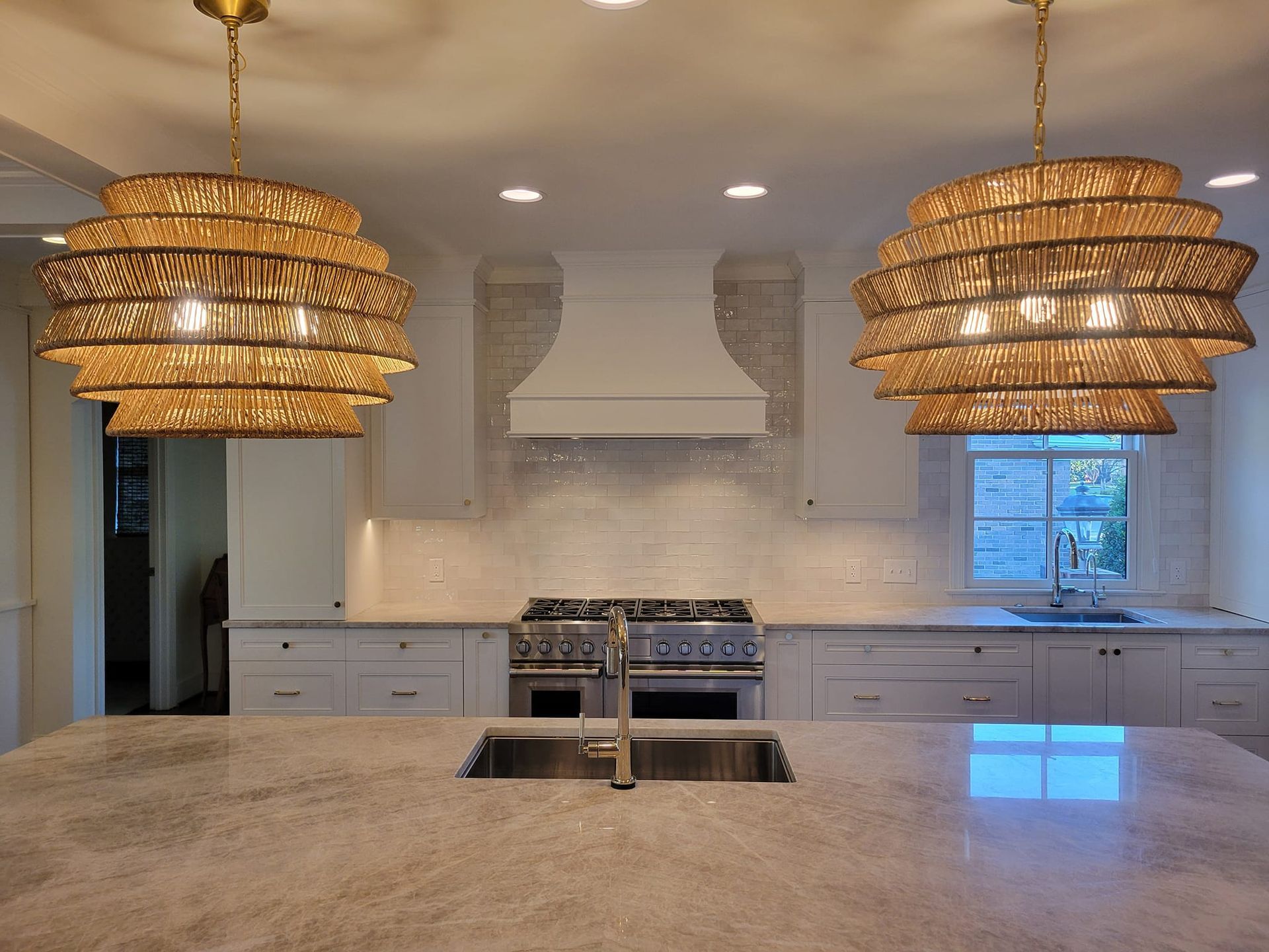 Modern kitchen with large island, white cabinets, stainless range, and woven pendant lights